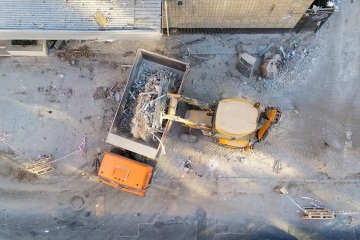 Bulldozer loader uploading waste and debris into dump truck at construction site. building dismantling and construction waste disposal service. Aerial drone industrial background
